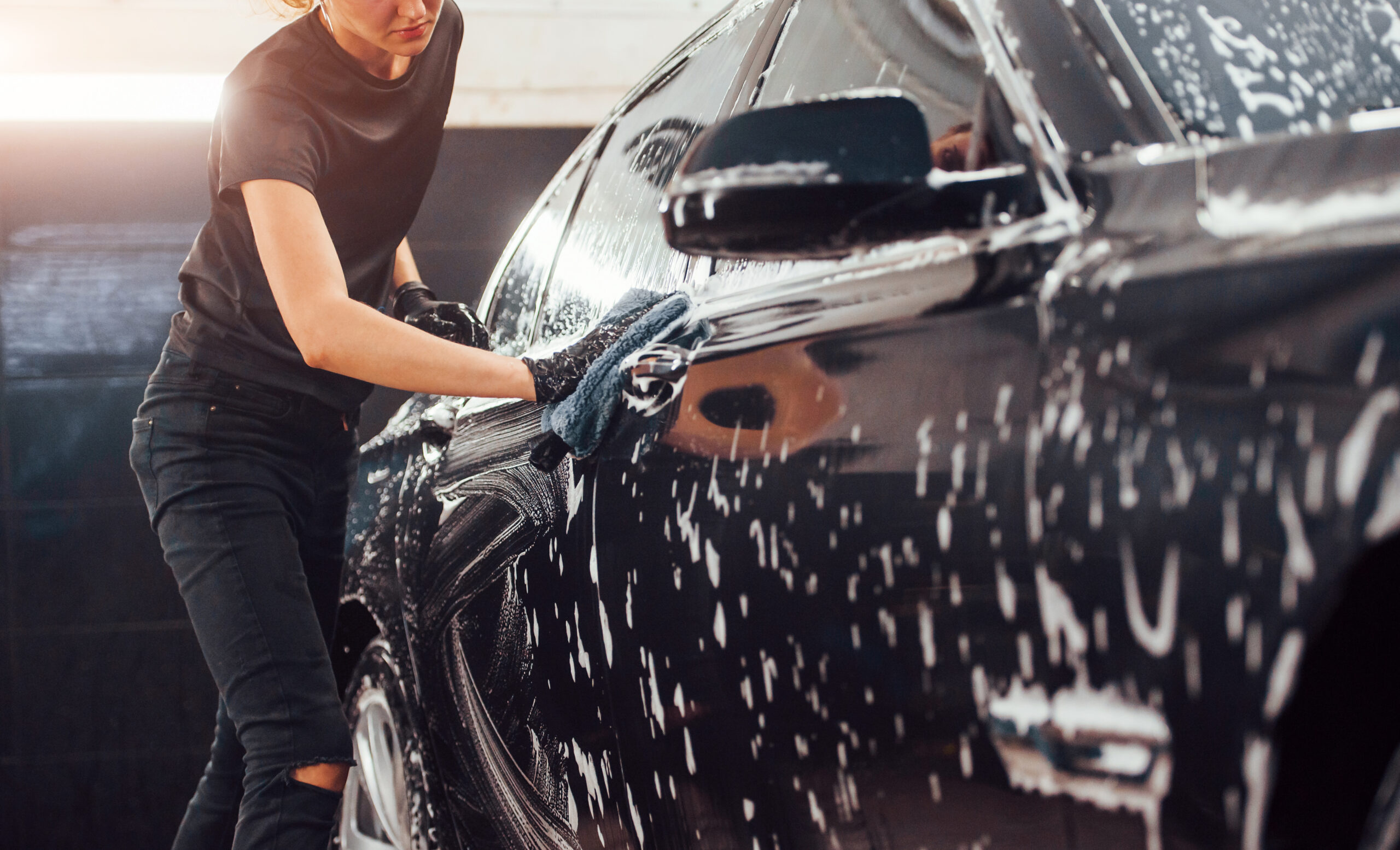 Woman washing a black vehicle with microfiber cloth during spring car cleaning in Leamington